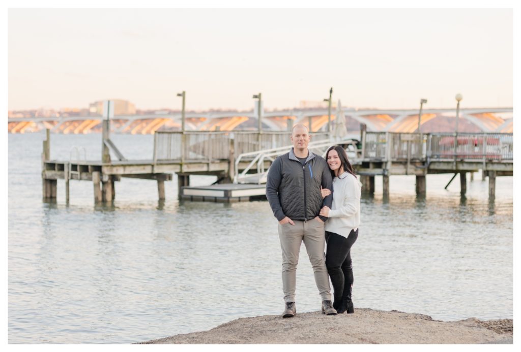 Winter Engagement Photos Alexandria VA Waterfront - couple hugging in front of dock and bridge